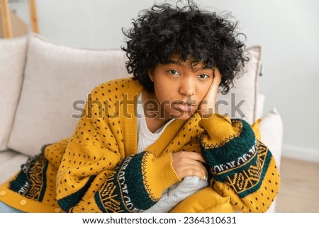 African american sad thoughtful pensive unmotivated girl sitting on sofa at home indoor. Young african woman ponder look tired after long day. Girl feels depressed offended lonely upset heartbreak