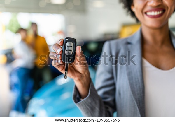 African American saleswoman holding key of\
new car. Customers in background.\
