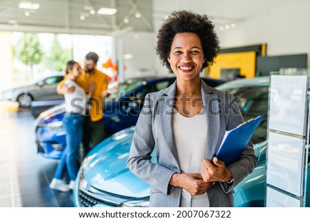 African American saleswoman working at car showroom. Customers in the background. 