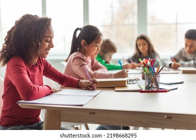 African American School Girl Writing Learning Sitting At Desk In Classroom Indoors. Diverse Children Having Class Taking Notes Indoor. Education And Knowledge. Selective Focus - Powered by Shutterstock