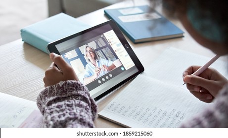 African American School Kid Child Girl Holding Digital Tablet Talking To Remote Teacher Tutor On Social Distance Video Conference Call Study Online Virtual Class Learning At Home, Over Shoulder View.