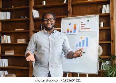 African American school teacher in glasses standing next to whiteboard with bar charts, explaining mathematics, streaming lesson online and looking at webcam, teaching in a virtual online classroom - Powered by Shutterstock