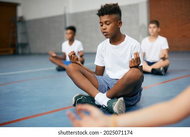 African American schoolboy and his friends meditating in lotus position during PE class at school gym. - Powered by Shutterstock