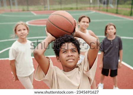 African American schoolboy holding ball over his head while throwing it into basket during basketball training before school competition