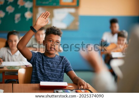 African American schoolboy raising his arm to answer teacher's question during class in the classroom.