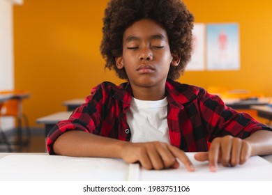 African american schoolboy sitting in classroom with eyes closed reading braille book with fingers. childhood and education at elementary school. - Powered by Shutterstock