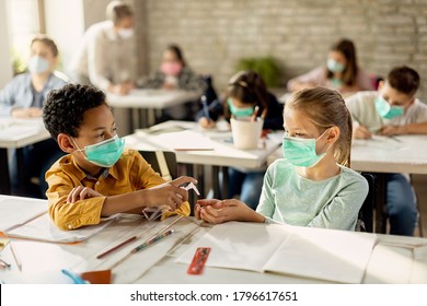 African American schoolboy spraying classmate's hands with disinfectant while wearing protective face masks on a class in the classroom.  - Powered by Shutterstock