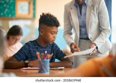 African American schoolboy studying with his teacher during a class at school. 