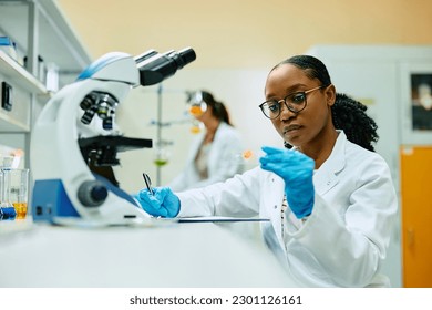 African American science student taking notes while analyzing test sample in a laboratory. - Powered by Shutterstock