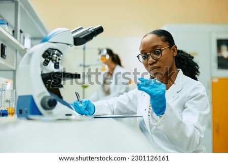 African American science student taking notes while analyzing test sample in a laboratory.