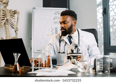 African American Scientist Doctor In White Coat Working With Microscope, Test Tubes In Laboratory, Making Notes On Laptop. Biotechnology, Medicine, Immunology, Microbiology Concept