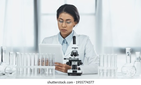 African American Scientist In Glasses Using Digital Tablet Near Microscope In Lab