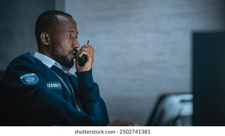 African American security officer or dispatch in uniform uses tablet computer and walkie talkie, looks at screens working in monitoring center during night shift. Surveillance and CCTV system concept. - Powered by Shutterstock