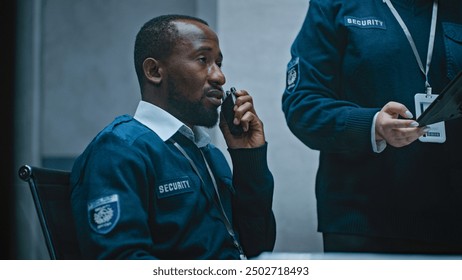 African American security officer talks in walkie talkie. Female coworker stands nearby and uses tablet computer. Multiethnic surveillance operators control CCTV cameras in modern monitoring center. - Powered by Shutterstock