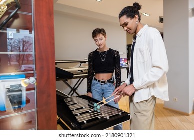 African American Seller Playing Xylophone Near Customer In Music Store