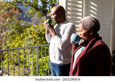 African american senior couple drinking coffee standing on balcony and looking into distance. retirement lifestyle, spending time at home and garden. - Powered by Shutterstock