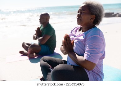 African american senior couple in prayer pose meditating while sitting at beach on sunny day. Unaltered, love, together, yoga, cross legged, retirement, nature, vacation and active lifestyle concept. - Powered by Shutterstock