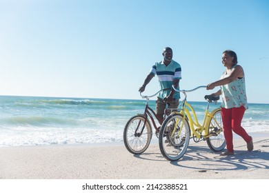 African american senior couple wheeling bicycles at beach against blue sky with copy space. unaltered, love, togetherness, active lifestyle, enjoyment and holiday concept. - Powered by Shutterstock