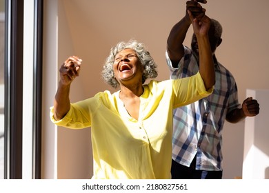 Hombre mayor afroamericano bailando con una alegre mujer contra la pared en casa de ancianos. Risa, amistad, unión, disfrute, sin alteraciones, recreación, apoyo, vida asistida y jubilación.