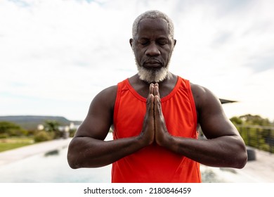 African american senior man with eyes closed meditating in prayer position against sky in yard. Yoga, zen, unaltered, support, assisted living, retirement home, fitness and active lifestyle concept. - Powered by Shutterstock