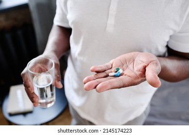 African American senior man with glass of water and three pills on hand going to take medicaments prescribed by his physician