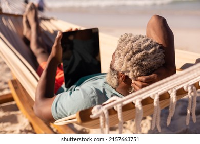 African american senior man with gray hair using digital tablet while lying on hammock at beach.  - Powered by Shutterstock