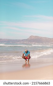 African American Senior Man With Gray Hair Crouching At Shore Against Blue Sky On Sunny Day. 