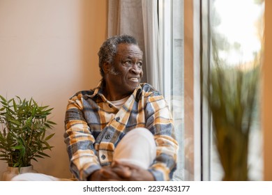 African American senior man looks through the window with depression, isolated at home. Sad mature man looking out the window - Powered by Shutterstock