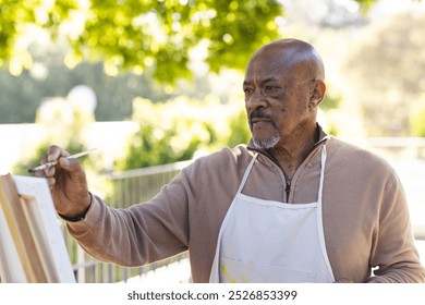 African american senior man painting on canvas on sunny terrace. Lifestyle, retirement, senior lifestyle, nature, creativity and domestic life, unaltered. - Powered by Shutterstock