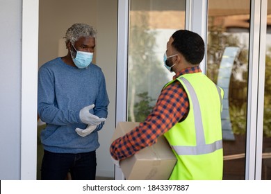 African American Senior Man Receiving Home Delivery Parcel, Wearing A Face Mask And Rubber Gloves. Social Distancing And Self Isolating At Home During Coronavirus Covid 19 Quarantine Lockdown.