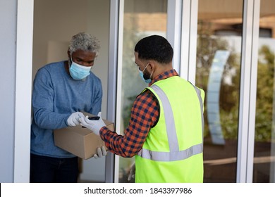 African American senior man receiving home delivery parcel, wearing a face mask and rubber gloves. Social distancing and self isolating at home during Coronavirus Covid 19 quarantine lockdown.