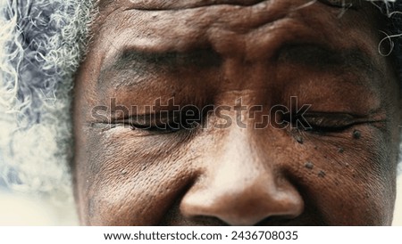 African American senior woman closing eyes in macro tight closeup. Wrinkled elderly lady meditating and praying, opening eyes with HOPE