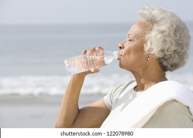 An African American senior woman drinking water from bottle with sea in the background - Powered by Shutterstock