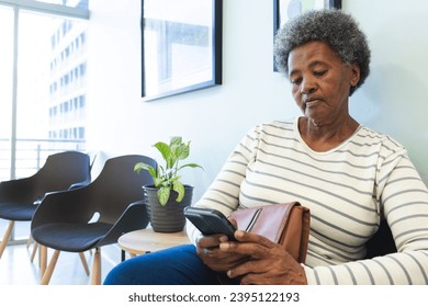 African american senior woman using smartphone in hospital waiting room. Medicine, healthcare, communication and medical services, unaltered. - Powered by Shutterstock