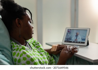 African American Sick Young Patient Resting In Bed Discussing Healthcare Treatment With Remote Physician Doctor During Online Videocall Meeting Conference. Telehealth Call On Tablet Screen