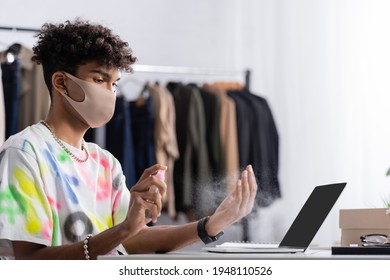 African American Small Business Owner In Protective Mask Spraying Hand Sanitizer Near Laptop