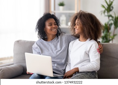 African American Smiling Mother And Teen Daughter Using Laptop, Having Fun Together At Home, Sitting On Couch, Smiling Mum Embracing Child, Shopping Online, Reading Funny News Or Watching Comedy