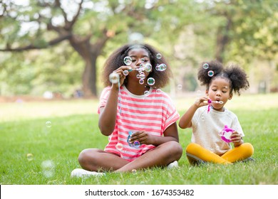 African American Children enjoying With Soap Bubbles In The City Park On Vacation Summer Day. Green Nature Background.