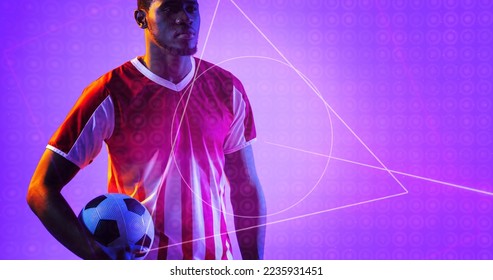 African american soccer player holding ball by geometric neon design over purple background. Computer graphic, copy space, digital composite, soccer, design, athlete, competitive sport. - Powered by Shutterstock