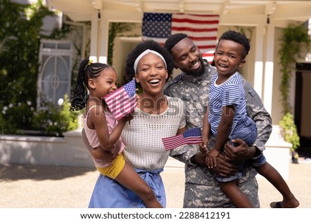 African american soldier husband and mother carrying children with flags of america outside house. Unaltered, family, togetherness, childhood, military, patriotism and homecoming concept.