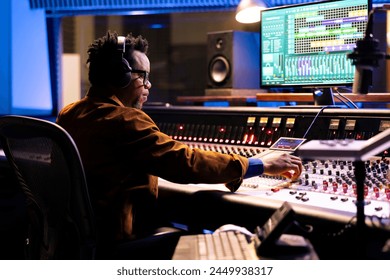 African american sound producer uses compressor and mixer in professional recording studio, adjusting volume levels and audio settings on a track. Music production concept in control room. - Powered by Shutterstock