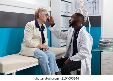 African american specialist doctor measuring temperature putting infrared thermometer on senior woman patient forehead discussing fever treatment. Medical appointment in hospital office - Powered by Shutterstock