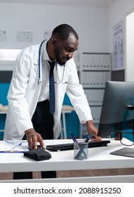 African american specialist doctor monitoring ill report on computer analyzing healthcare treatment during clinical appointment. Physician man working at medical expertise in hospital office