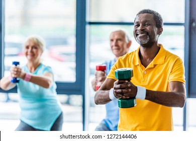 african american sportsman and his friends exercising with dumbbells at gym
