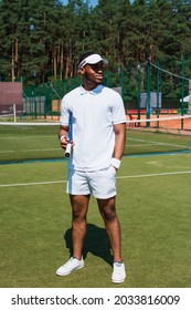 African american sportsman holding tennis racket and hand in pocket on court