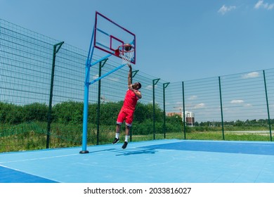 African american sportsman jumping under hoop and ball on basketball playground