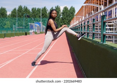 African American Sportswoman Stretches Legs On Running Track. Black Runner Prepares To Train For Competition On Jogging Track To Show Perfect Results. Black Woman Ready To Run On Red Racetrack 