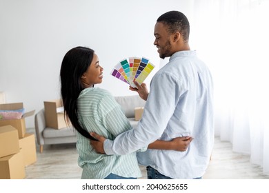 African american spouses choosing color for walls painting, holding palette and looking at each other, standing back to camera at home. Renovation planning concept