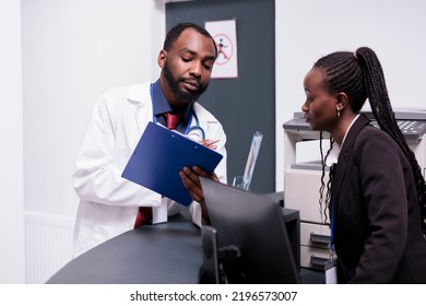 African american staff working on medical reports at hospital reception desk, analyzing patients appointments on papers. Doctor and receptionist using checkup forms to help people with disease. - Powered by Shutterstock