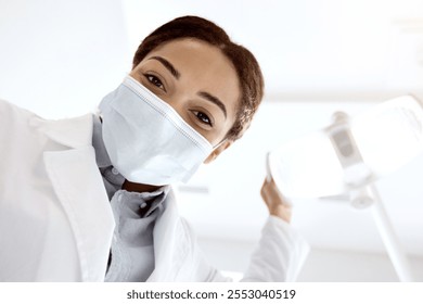 African American Stomatologist Lady Adjusting Medical Lamp Before Check Up With Patient, Professional Black Dentist Doctor Woman Wearing Protective Medical Mask Ready For Dental Treatment, Low Angle - Powered by Shutterstock